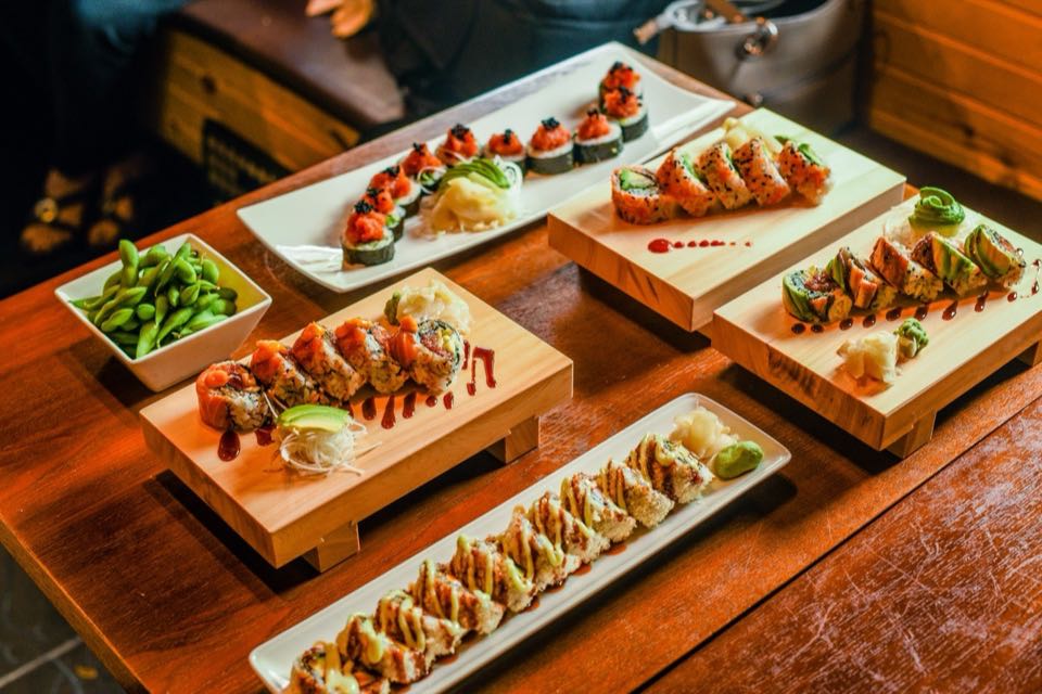 Assorted specialty sushi rolls on wooden boards with edamame at Amarit