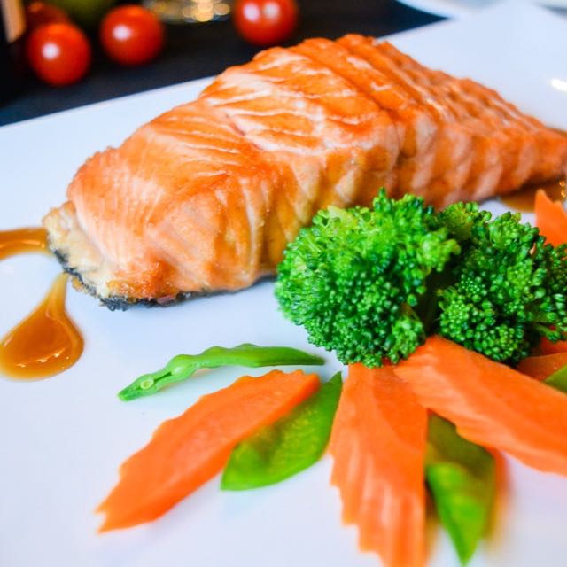 Grilled salmon with broccoli, snow peas and carrots on a white plate