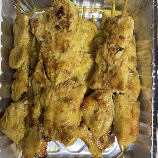 Ten grilled chicken satay skewers in a foil takeout tray