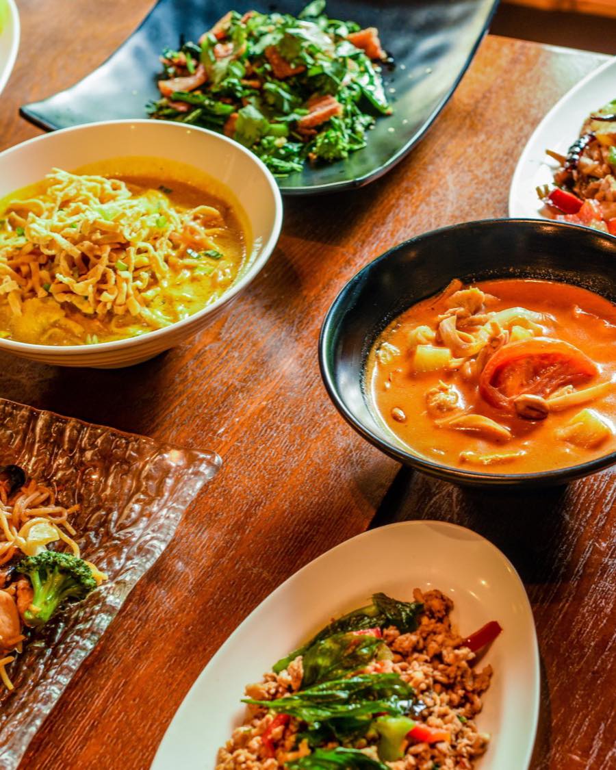 Table spread of Thai dishes at Amarit including khao soi, red curry, pad see ew and basil stir-fry