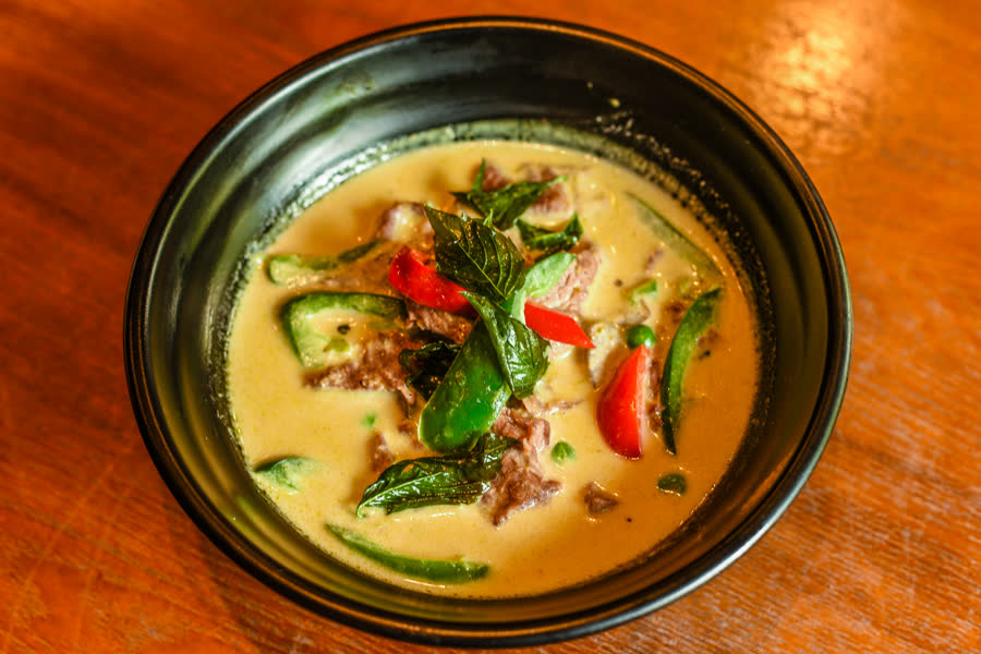 Green curry with beef, bell pepper and basil in a black bowl